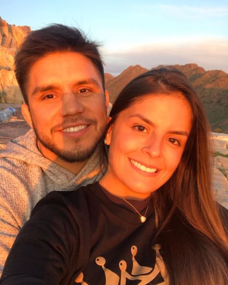 Henry Cejudo in a grey hoodie poses a picture with girlfriend Amanda Dallago Chaves.